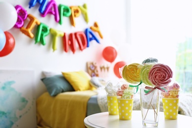 Photo of Table with treats and phrase HAPPY BIRTHDAY made of colorful balloon letters in modern bedroom. Space for text