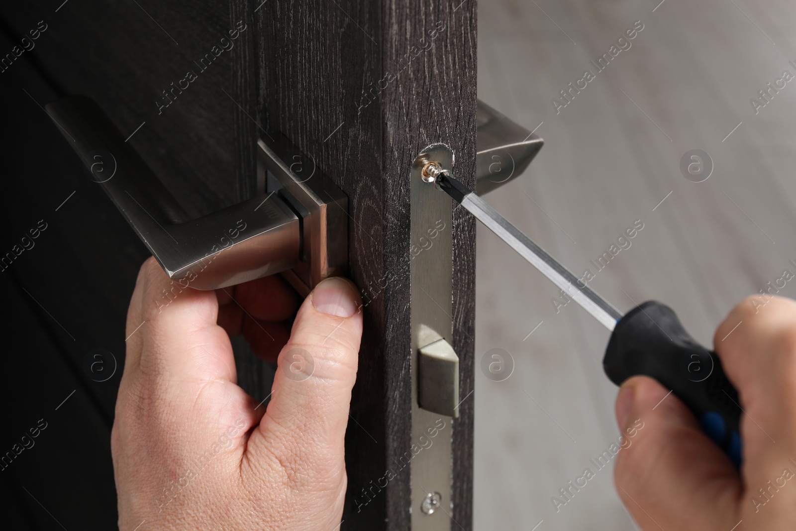 Photo of Handyman with screwdriver repairing door handle indoors, closeup