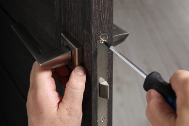 Photo of Handyman with screwdriver repairing door handle indoors, closeup