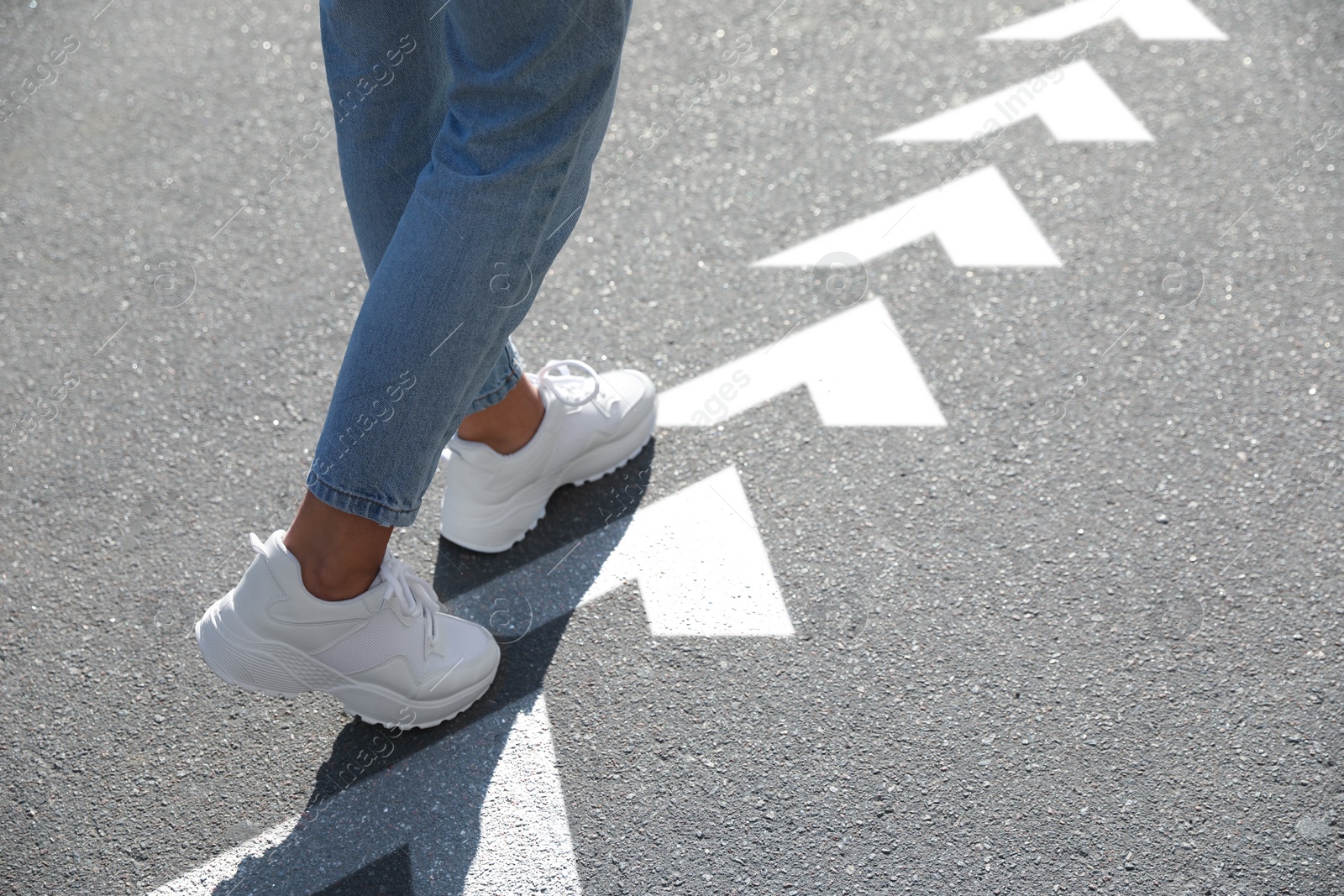 Image of Planning future. Woman walking on drawn marks on road, closeup. White arrows showing direction of way