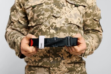 Soldier in military uniform holding medical tourniquet on light grey background, closeup