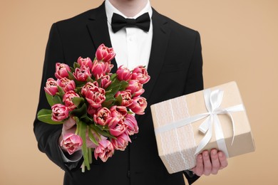 Man with beautiful bouquet and present on beige background, closeup