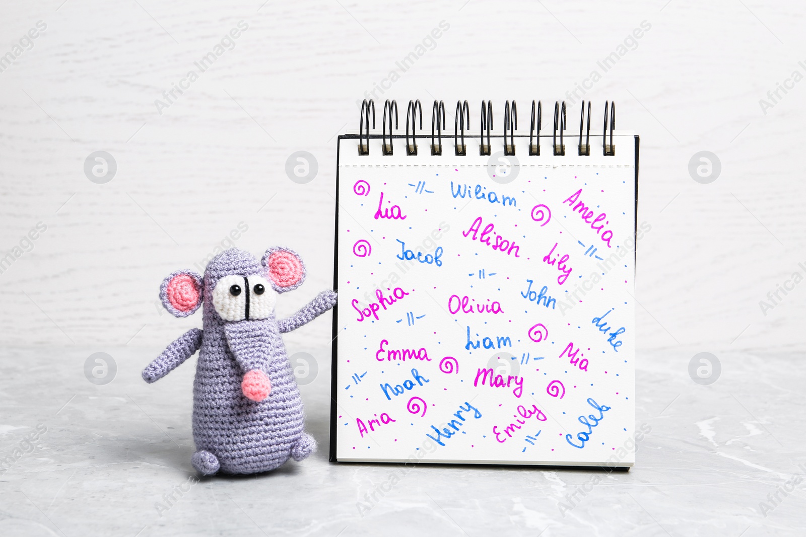 Photo of Notebook with different baby names and toy on grey marble table against white background