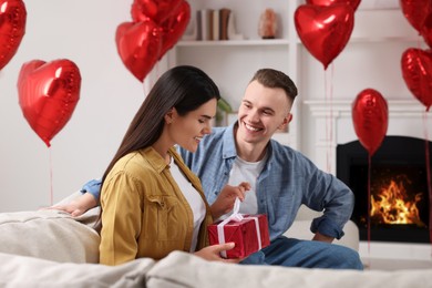 Photo of Woman opening gift from her boyfriend indoors. Valentine's day celebration