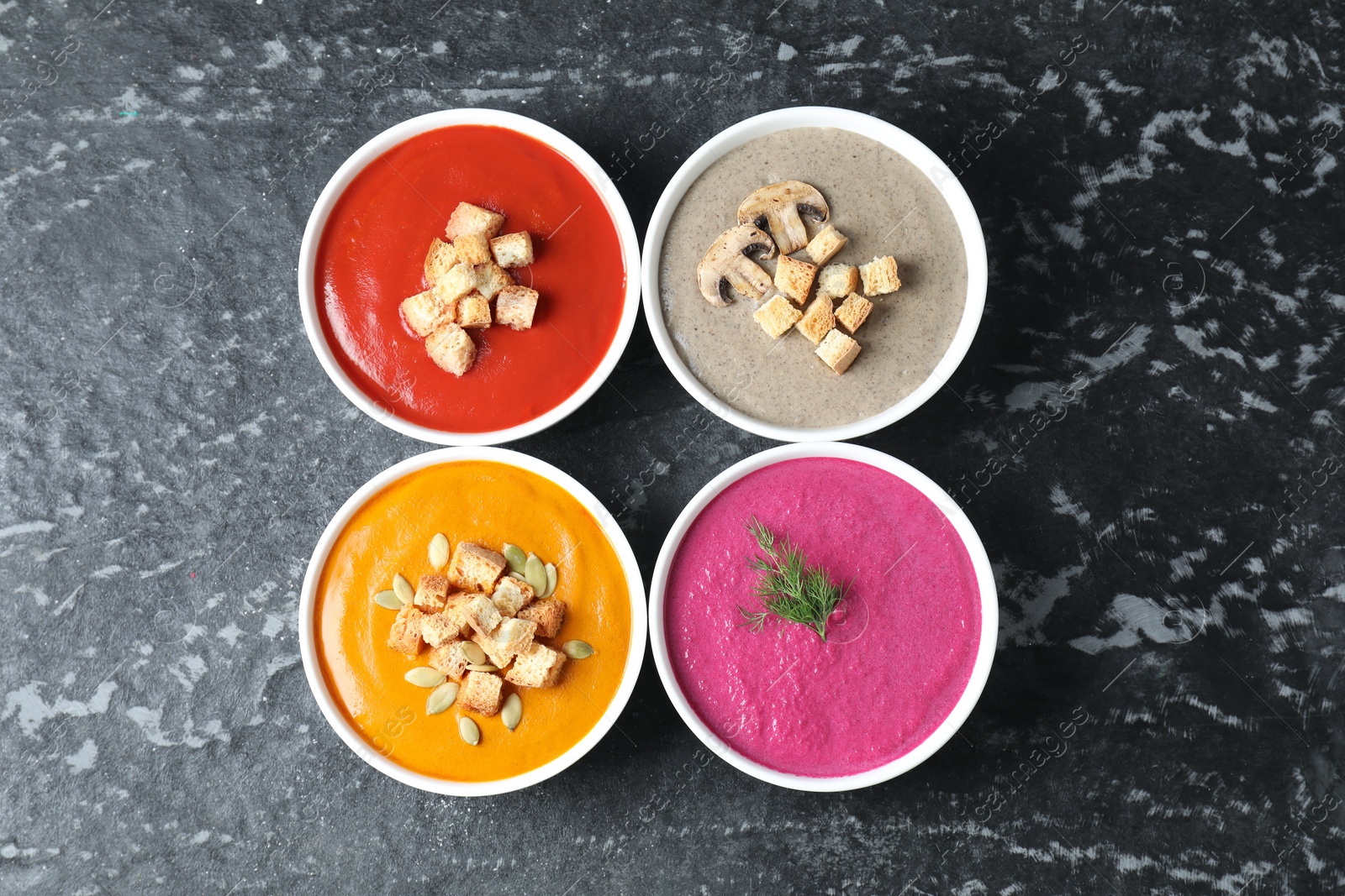 Photo of Different tasty cream soups in bowls on black textured table, flat lay