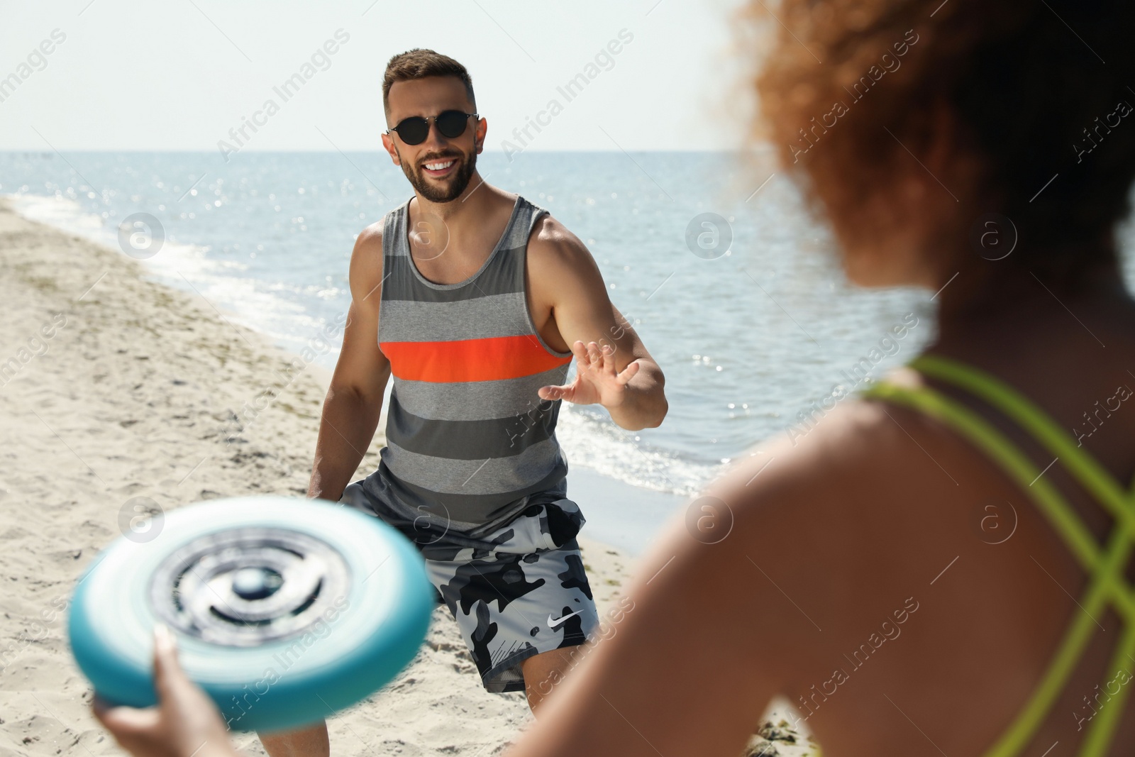 Photo of Couple playing with flying disk at beach on sunny day