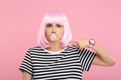 Photo of Beautiful woman blowing bubble gum and pointing at herself on pink background