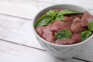 Photo of Bowl with raw chicken liver and basil on white wooden table, closeup. Space for text