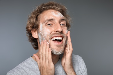 Photo of Young man washing face with soap on grey background