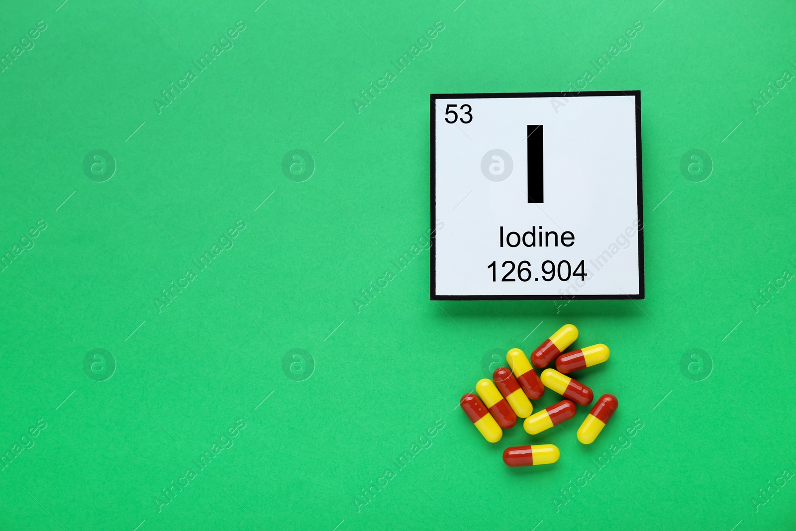Photo of Card with iodine element and pills on green background, flat lay. Space for text