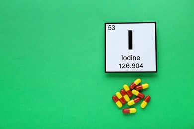 Card with iodine element and pills on green background, flat lay. Space for text