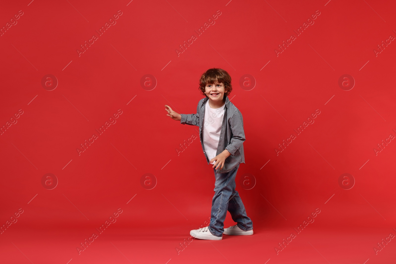 Photo of Happy little boy dancing on red background. Space for text