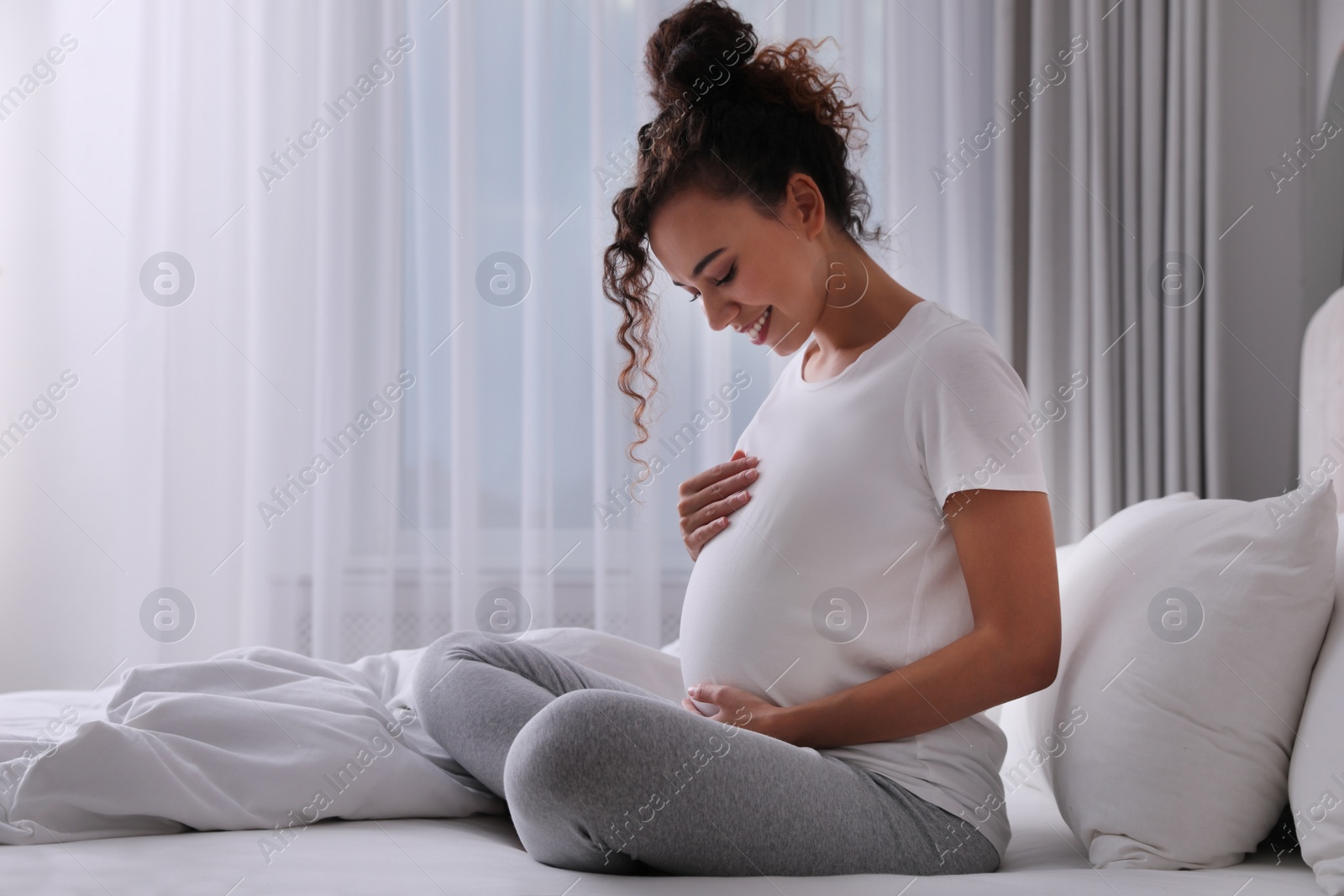 Photo of Pregnant young African-American woman sitting on bed at home