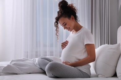 Photo of Pregnant young African-American woman sitting on bed at home