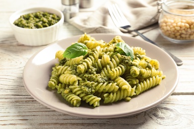 Photo of Plate with delicious basil pesto pasta on wooden table