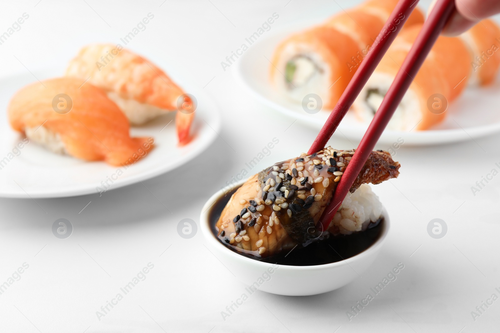 Photo of Dipping tasty nigiri sushi with smoked eel into soy sauce on white table, closeup