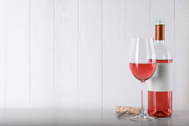 Corkscrew near bottle and glass of delicious rose wine on table against white wooden background. Space for text