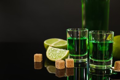 Photo of Absinthe in shot glasses, brown sugar, lime and spoon on mirror table, space for text. Alcoholic drink