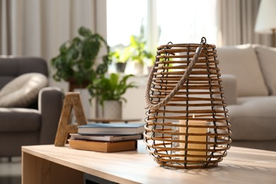 Stylish holder with burning candle and books on wooden table in living room. Space for text