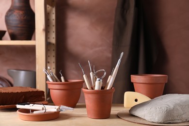 Photo of Clay and set of modeling tools on wooden table in workshop