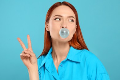 Photo of Beautiful woman blowing bubble gum and showing peace gesture on turquoise background