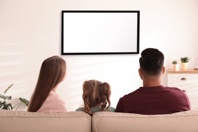 Family watching TV on sofa at home, back view