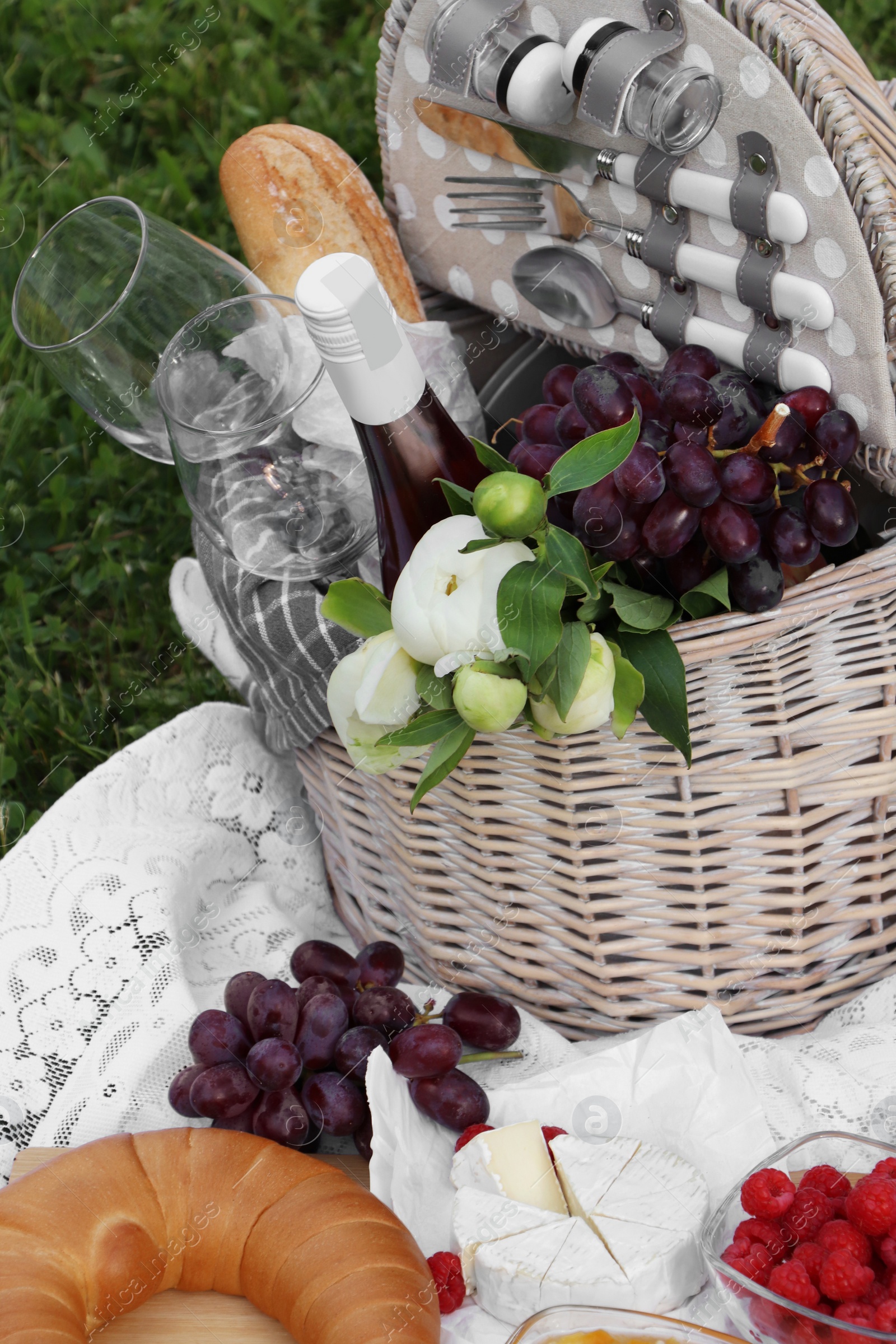 Photo of Picnic blanket with tasty food, flowers, basket and cider on green grass outdoors