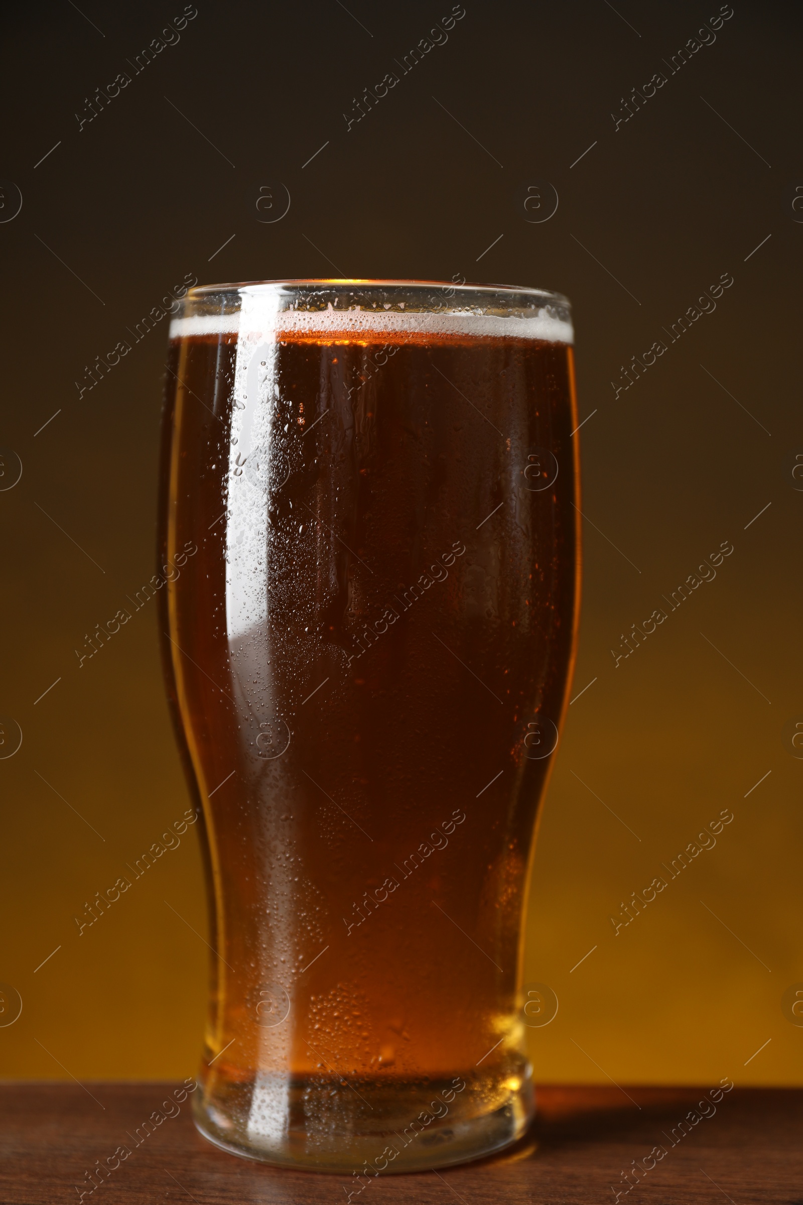 Photo of Glass with fresh beer on wooden table against dark background