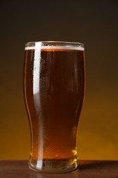Glass with fresh beer on wooden table against dark background