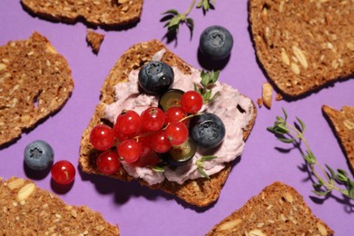 Tasty sandwich with cream cheese, blueberries and red currants on lilac background, flat lay