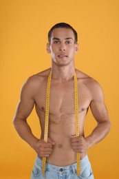 Photo of Handsome shirtless man with slim body and measuring tape on yellow background