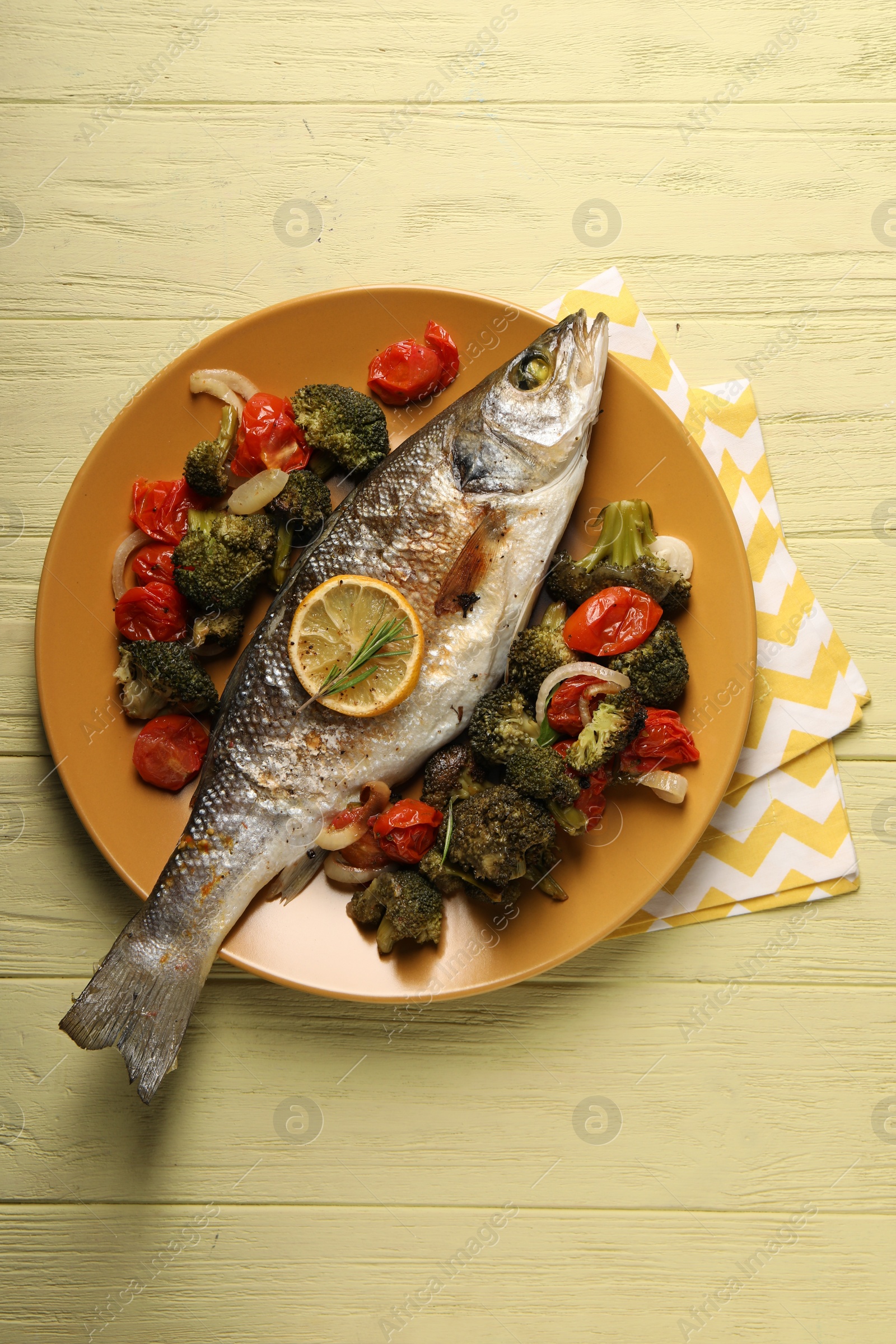 Photo of Delicious baked fish and vegetables on yellow wooden table, top view