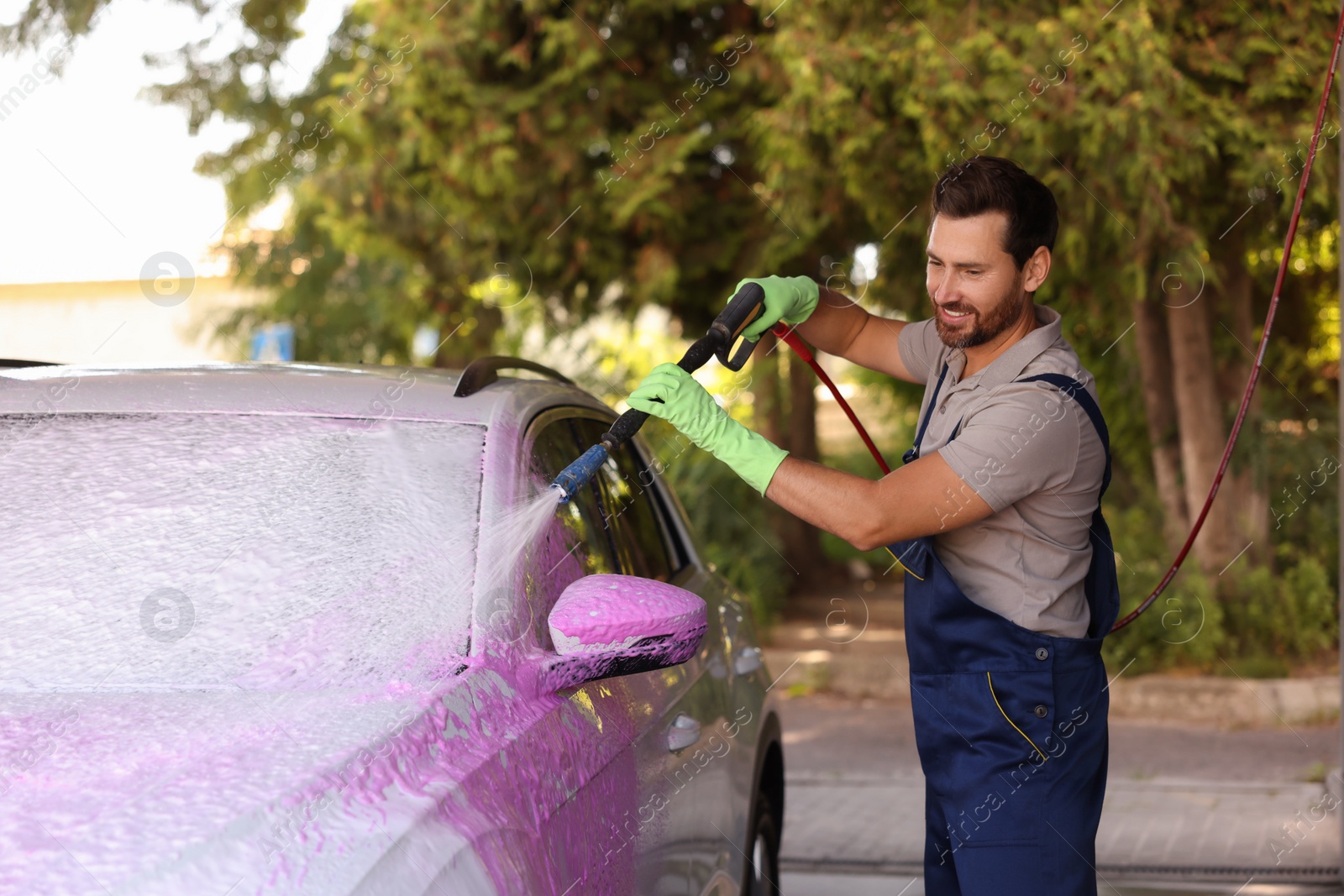 Photo of Worker washing auto with high pressure water jet at outdoor car wash