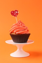 Photo of Delicious cupcake with bright cream and heart topper on orange background