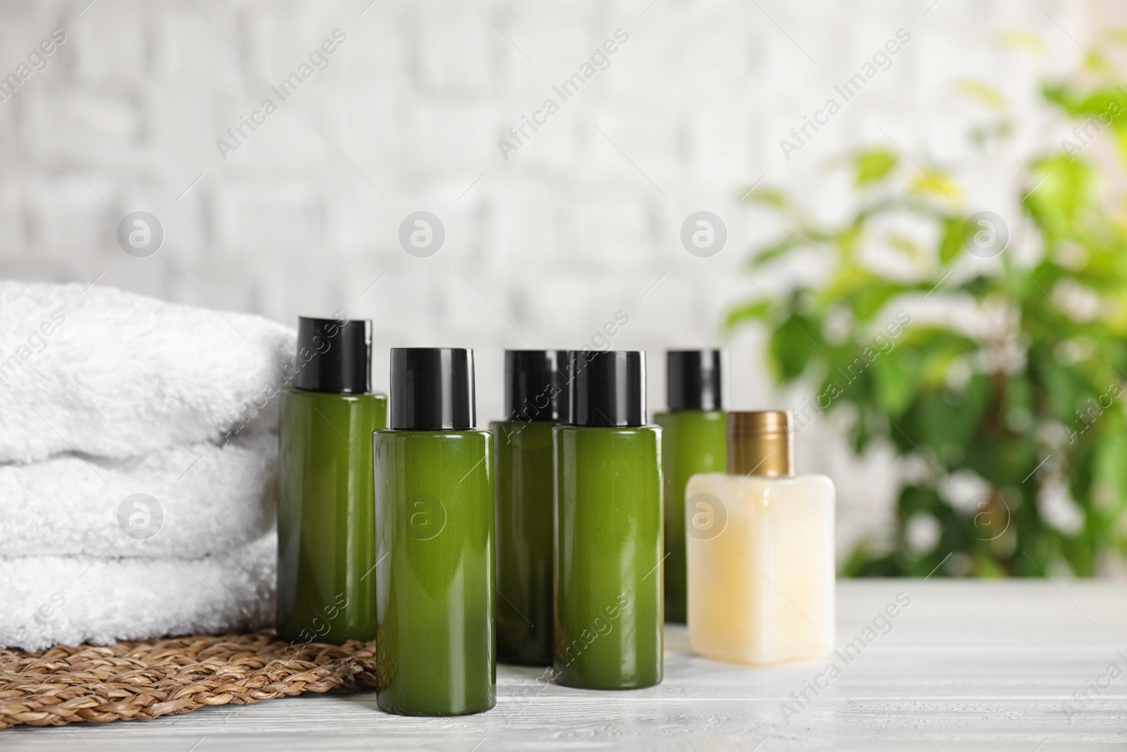 Photo of Mini bottles with cosmetic products and towel on white wooden table