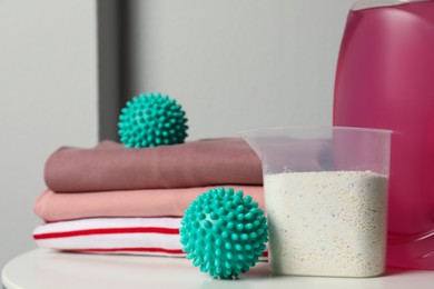 Photo of Turquoise dryer balls, detergents and stacked clean clothes on white table