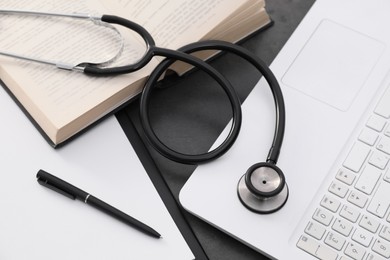 Photo of Open student textbook, clipboard and stethoscope near laptop on grey table, above view. Medical education