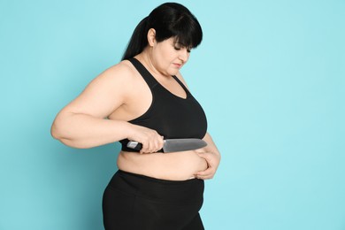 Photo of Obese woman with knife on light blue background. Weight loss surgery