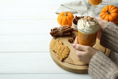 Photo of Woman holding cup of tasty pumpkin spice latte with whipped cream at white wooden table, closeup. Space for text