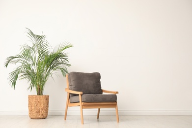 Photo of Stylish room interior with wooden armchair and houseplant near light wall. Space for text