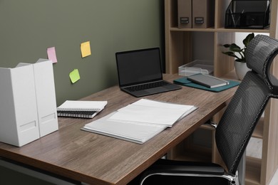 Photo of Folder with punched pockets and laptop on wooden table in office