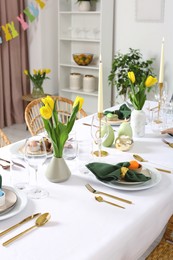 Photo of Festive Easter table setting with painted eggs, burning candles and yellow tulips in room