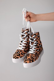 Photo of Woman holding pair of sneakers with leopard print on light grey background, closeup