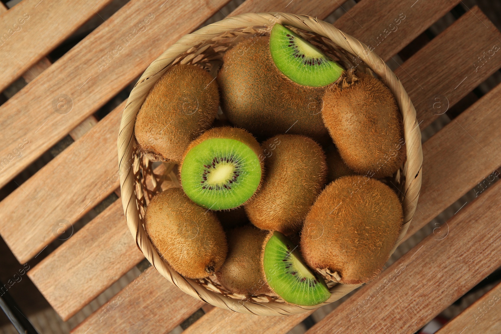 Photo of Wicker basket with whole and cut kiwis on wooden table, top view