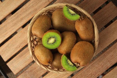 Photo of Wicker basket with whole and cut kiwis on wooden table, top view