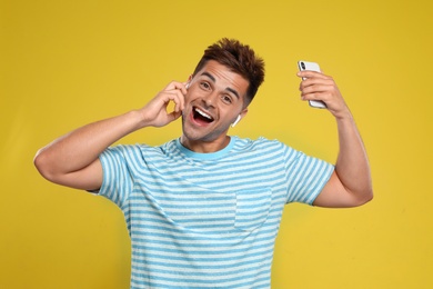 Photo of Happy young man with smartphone listening to music through wireless earphones on yellow background