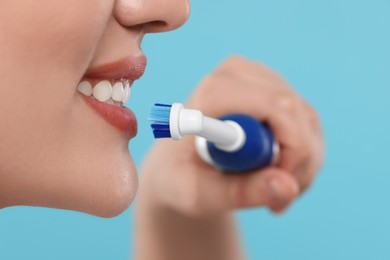Photo of Woman brushing her teeth with electric toothbrush on light blue background, closeup