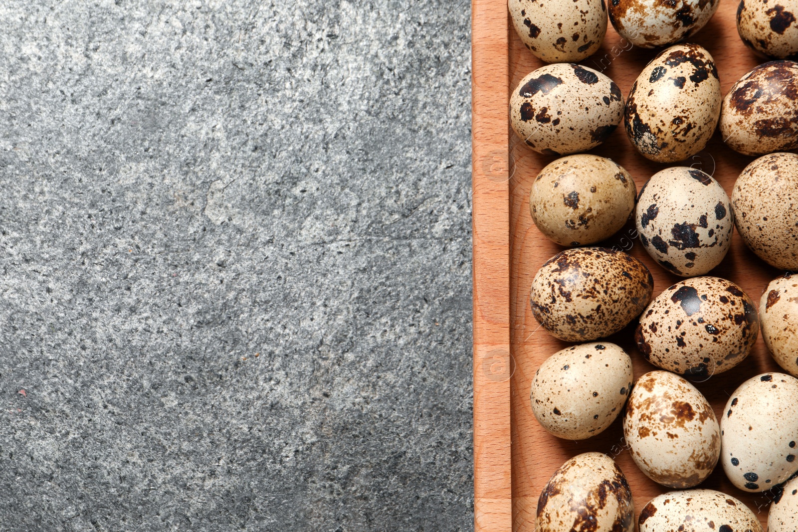 Photo of Wooden tray with quail eggs on grey table, top view. Space for text