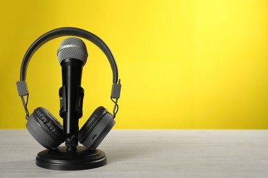 Photo of Microphone and modern headphones on white wooden table against yellow background, space for text