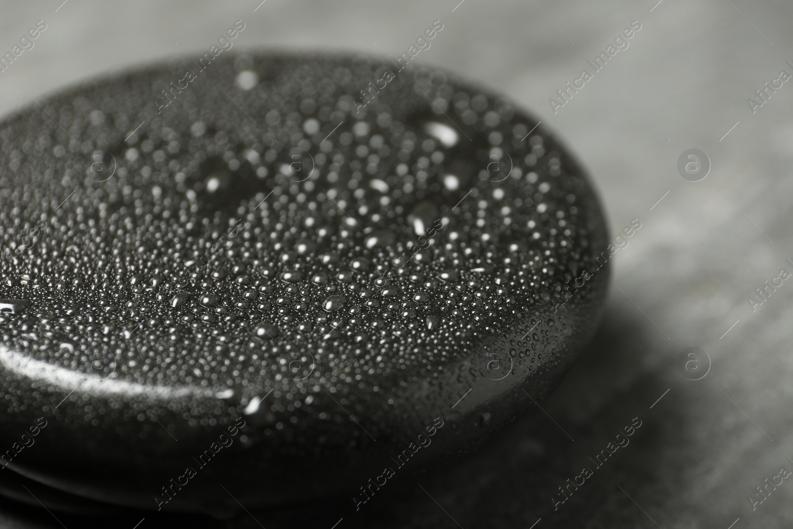 Photo of Wet black spa stone on grey table, closeup